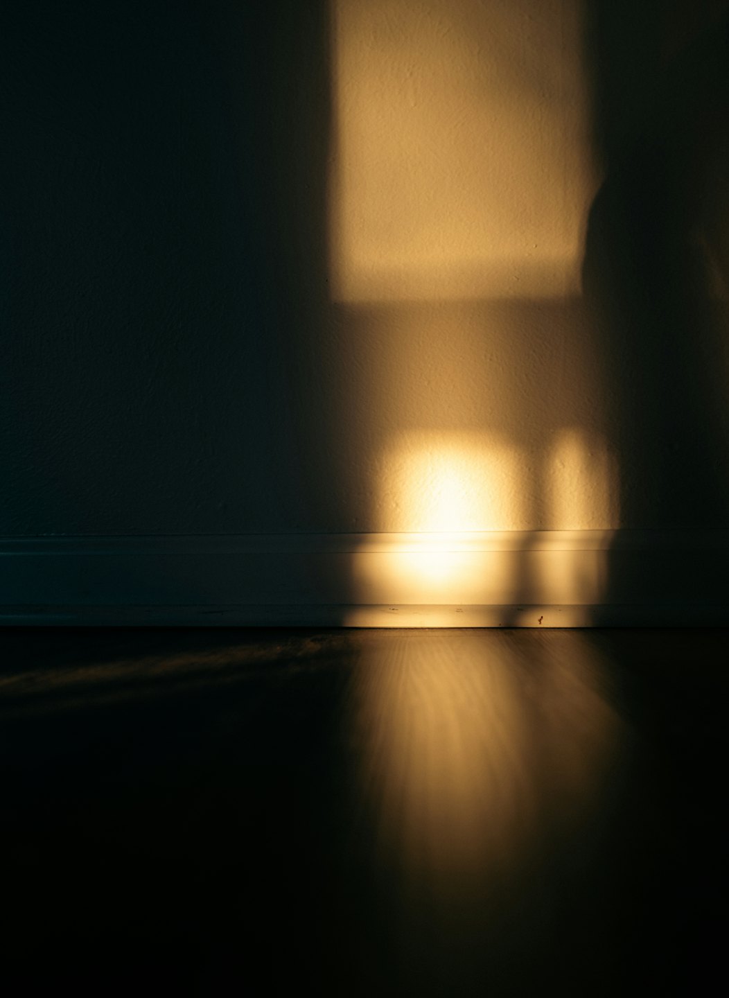 Sunlight casts rectangular patterns onto a wooden floor and wall.